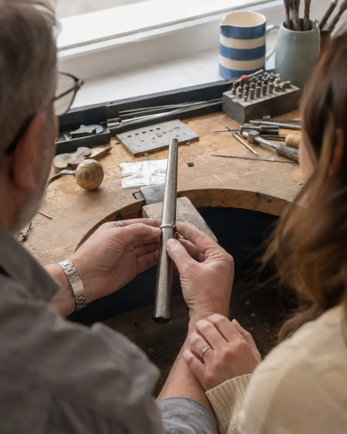 A craftsman guiding a couple as they size a wedding ring in the workshop